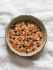 Apricots, cherries, strawberries crumble in a baking dish on a light background, top view