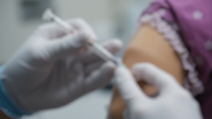 Fototapeta premium Blurry image of a medical worker wearing gloves while administering a vaccination. Concepts of vaccination, safety, medical care, and the hospital environment with a shallow depth of field.