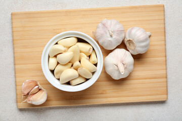 Wooden board with fresh garlics and bowl of cloves on white background