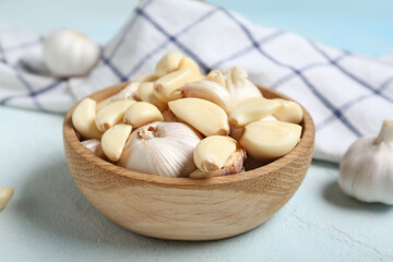 Wooden bowl with fresh garlics on light blue background, closeup