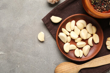 Wooden plate with fresh garlic cloves and bowl of peppercorns on grey background