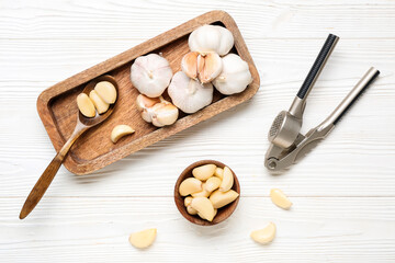 Tray with fresh garlics and bowl of cloves on white wooden background