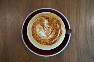 Close up red ceramic mug cup of hot Latte art coffee on wooden table
