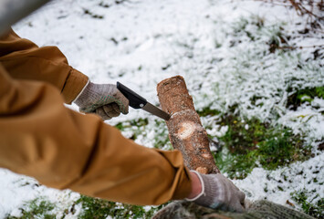 Person sawing Christmas tree trunk outdoors in snowy garden, winter holiday preparation