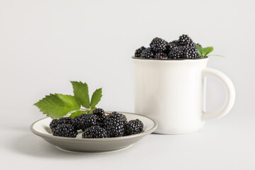 Plate and cup with sweet ripe blackberries on grey background