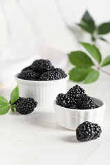 Bowls with sweet ripe blackberries and leaves on white background