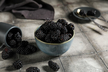Bowl and cup with sweet ripe blackberries on grey tile background