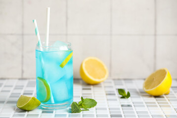 Glass of tasty Blue Lagoon cocktail with lime and mint on grey tile table