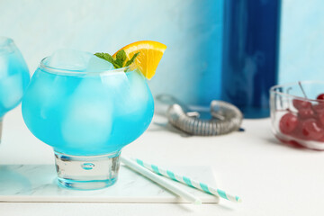Glass of tasty Blue Lagoon cocktail garnished with orange and mint on white table