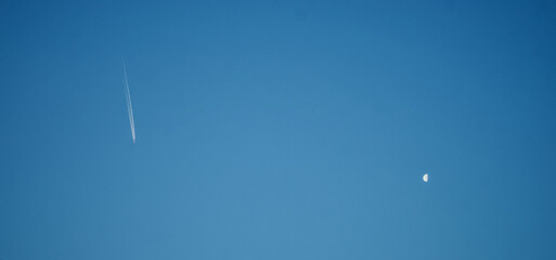 Flying airplane trace smoke and the half moon in the blue sky