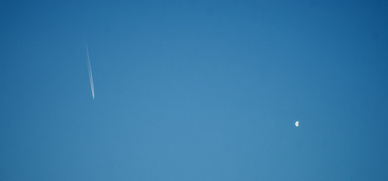 Flying airplane trace smoke and the half moon in the blue sky - Powered by Adobe