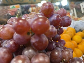 Close view shows ripe red globe grapes with oranges blurred in background