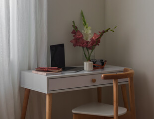 Laptop, notebooks, cup of coffee, bouquet of gladioli on the white table in the living room