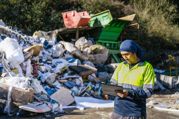 Waste management worker using clipboard to inspect and monitor garbage and trash at a landfill site, ensuring proper waste disposal and recycling procedures
