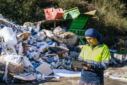 Waste management worker using clipboard to inspect and monitor garbage and trash at a landfill site, ensuring proper waste disposal and recycling procedures