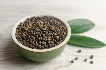 Green coffee beans in a bowl with green leaves on a white wooden table. Alternative drink concept. Selective focus. Horizontal orientation.