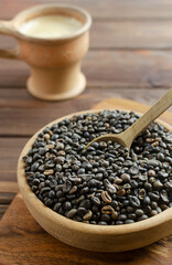 Green coffee beans in a wooden bowl with a ceramic coffee cup on a brown table. Alternative drink concept. Rustic style. Selective focus. Vertical orientation.