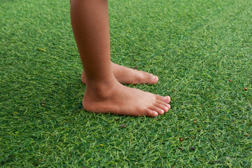 Bare feet of child standing on synthetic green grass in garden