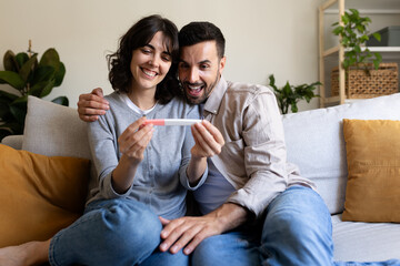 Happy, surprised couple looking at positive pregnancy test.