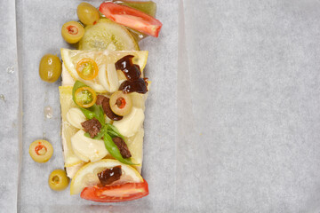 A top-down shot showcases a piece of tofu with layered seaweed, topped with fresh vegetables and lemon, prepared for baking on parchment paper