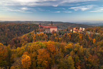 Książ Castle seen from above in autumn, wrapped in golden and red trees, rising over the forested landscape, blending history with natural beauty in Lower Silesia, Poland.