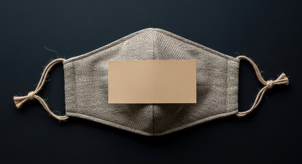 Face covering with blank card on dark surface top view