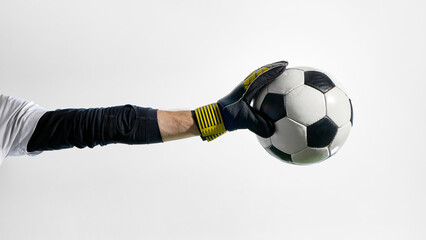 Goalkeeper holding soccer ball in gloved hand with extended arm. Concept of goalkeeping visuals, defensive technique, sports education, game rules content, training focus.
