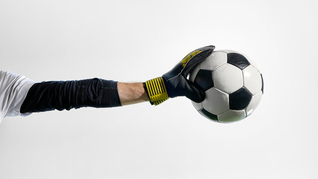 Goalkeeper holding soccer ball in gloved hand with extended arm. Concept of goalkeeping visuals, defensive technique, sports education, game rules content, training focus. - Powered by Adobe