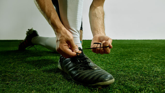 Male football player kneeling and tying shoelaces before game. Concept of game preparation, focus, strength, team discipline, youth football gear and sport routine.