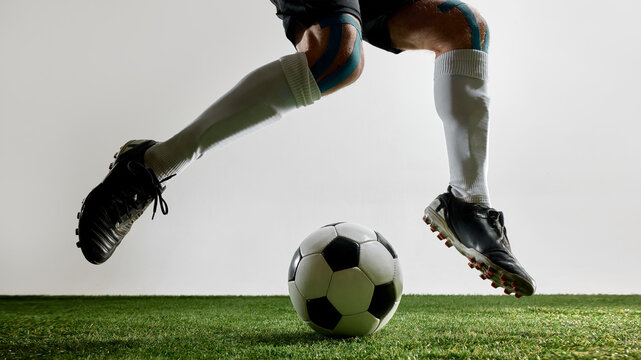 Football player jumping with feet above ball on green turf. Concept of sport technique, jump training, youth energy, brand visuals, and football fitness.