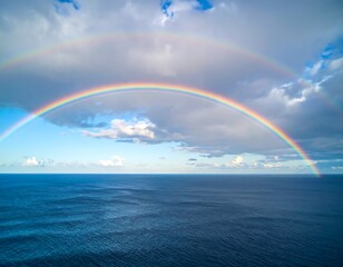 Double rainbow arcing over a calm ocean under a partly cloudy sky