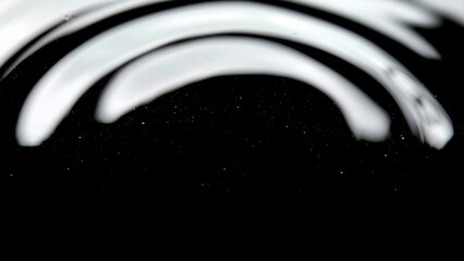 Abstract shot of a blurred water surface, creating graceful, sweeping arcs of light and shadow against a dark background