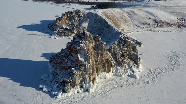 Aerial view of jagged rocks covered in white snow, standing starkly against the snowy landscape, creating a striking contrast, Irkutsk Oblast, Russia.
