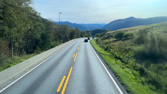Elevated personal POV traveling E39 road near Vikesa, Norway, personal perspective looking through front window. Approaching road bend in mountainous area.