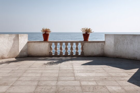 A vacant balcony featuring three stone railings decorated with terracotta pots, framed by angular concrete walls, with a view of the ocean.
