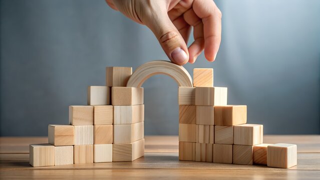 A hand places the final piece to complete a bridge made of wooden blocks, symbolizing connection and problemsolving