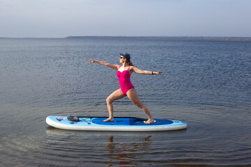 Woman doing yoga on sup board at sunset, outdoor summer activity. Sup yoga. Social Distancing. copy space. Mental Health