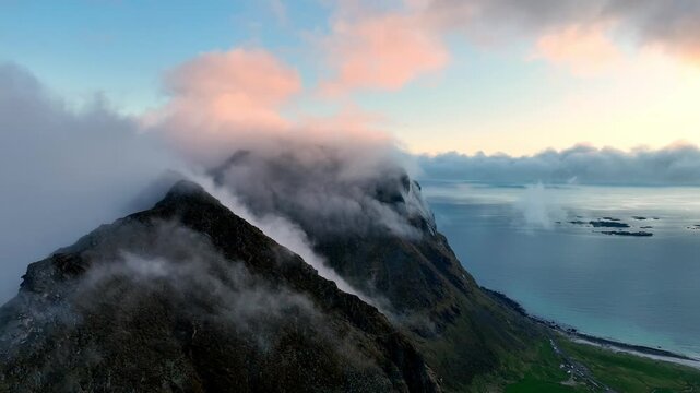 Fog wraps Mannen peaks as ocean fog climbs over mountains and Utakleiv glows in pink midnight sun in Lofoten