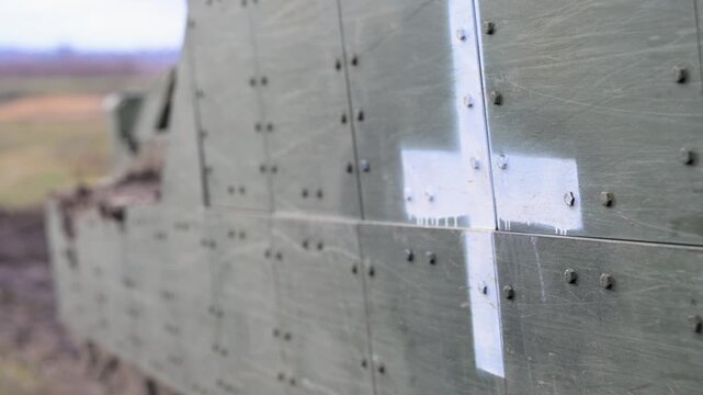 A close-up of a white cross stenciled on the side of an M2 Bradley IFV in Ukraine. This marking designates the fighting vehicle for a life-saving casualty evacuation (CASEVAC) role.