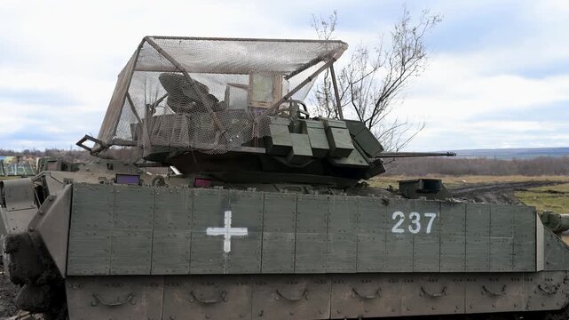 A shot of a US-made M2 Bradley IFV in Ukraine, a white medical cross, and an overhead 'cope cage' for protection against drones.