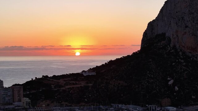 Aerial view of beautiful sunset over rocky cliff near calm coastal place with Estimar hotel, Calp, Alicante, Spain.