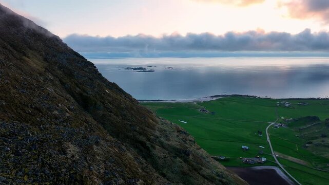 Aerial near Mannen wall reveals Utakleiv and mountain top wrapped in ocean fog at midnight sun