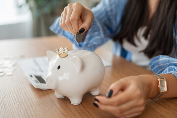 close up on adult woman hands put coins at piggy bank