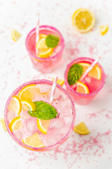 A cold pink refreshing drink with lemon and mint, chilled with ice cubes, decorated with a pink sugar rim. The best summer drink, rose lemonade on white background.