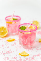 A cold pink refreshing drink with lemon and mint, chilled with ice cubes, decorated with a pink sugar rim. The best summer drink, rose lemonade on white background.
