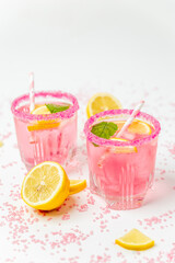 A cold pink refreshing drink with lemon and mint, chilled with ice cubes, decorated with a pink sugar rim. The best summer drink, rose lemonade on white background.