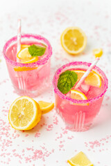 A cold pink refreshing drink with lemon and mint, chilled with ice cubes, decorated with a pink sugar rim. The best summer drink, rose lemonade on white background.
