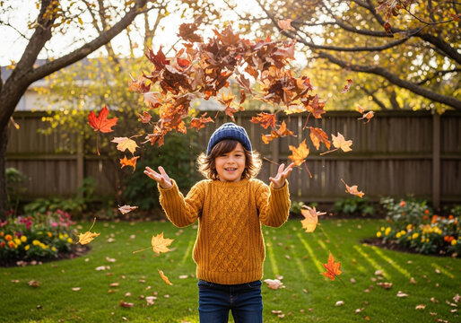 Joyful young boy in mustard sweater and blue beanie tossing autumn leaves in a sunlit backyard. - Powered by Adobe