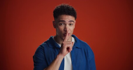 Face, whisper and man with silence in studio for gossip, confidential information and secret. Mockup space, person and hush emoji on red background for private news, mystery announcement and rumor