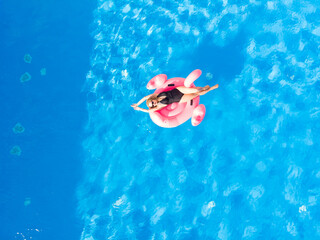 Woman on flamingo pool float in pool, drone aerial view. Summer holidays